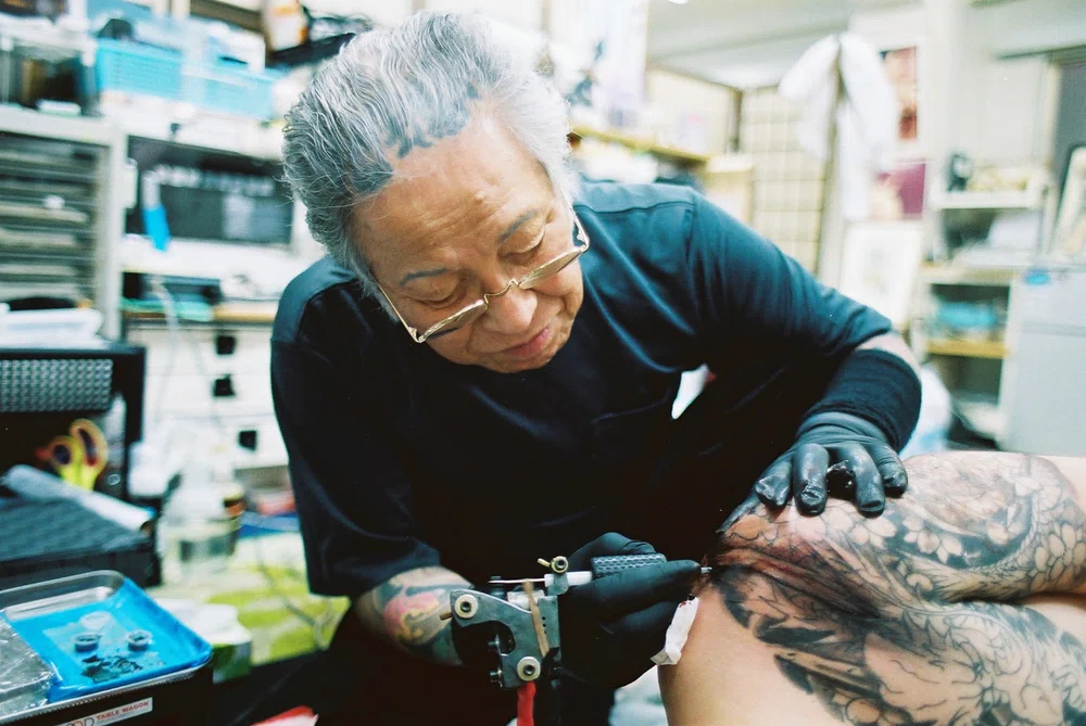 Artista de tatuaje Horiyoshi III realizando un tatuaje en la piel de un cliente. Cultura del tattoo en Japón.