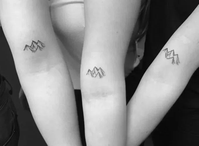 3 brazos juntos tatuados. Dibujo de un paisaje, montañas, tatuadas en el brazo de 3 mujeres. Técnica de micro tattoo
