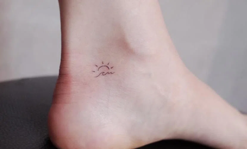mini tatuaje en el pie. Dibujo de sol y olas tatuados en interior de tobillo