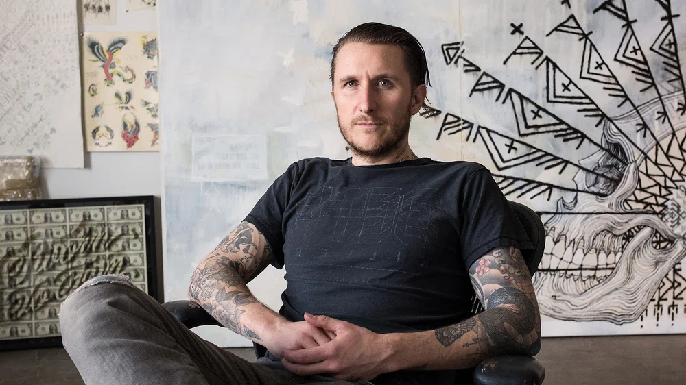 fotografía de scott campbell, tatuador profesional, sentado en una silla en su estudio de tatuaje.