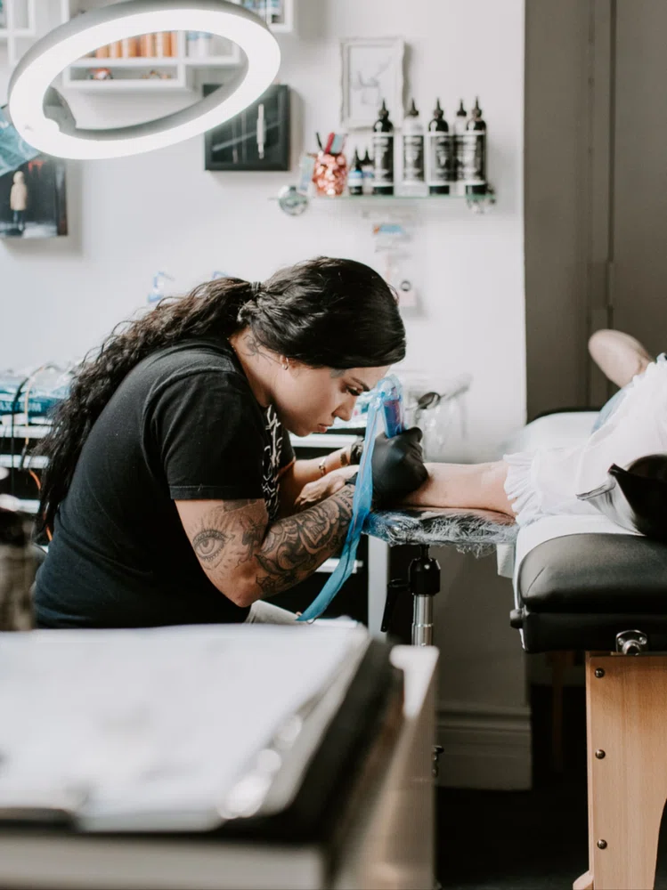Tatuadora profesional realizando un trabajo a un cliente en su estudio de tatuaje