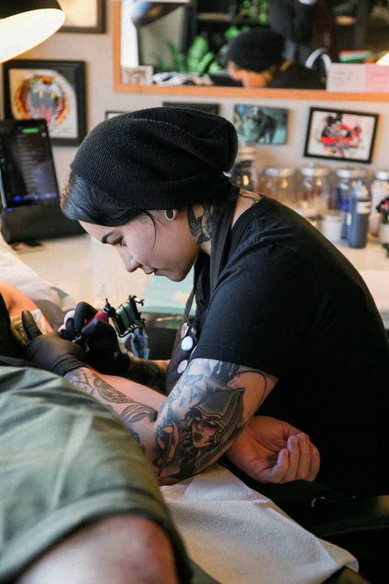 Tatuadora tatuando un diseño en el brazo de un hombre